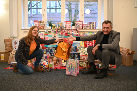 Jochen Drescher, Kanzler der Fachhochschule, überreicht der Beschäftigten Miriam Hobohm seinen Beitrag für den „Geschenkeschlitten“. Bild der Geschenke auf einem Schlitten
