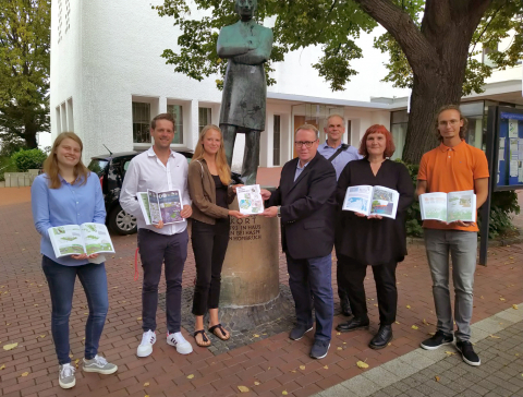 Fünf Studierende haben ihre 55 Ideen für den Stadtbezirk Hombruch in gebundener Form gemeinsam mit Prof. Christian Moczala an Bezirksbürgermeister Nils Berning (Mitte) übergeben. Die Dokumentation der Projektideen ist frei erhältlich. Menschen präsentieren das Buch auf dem Markt in Hombruch.